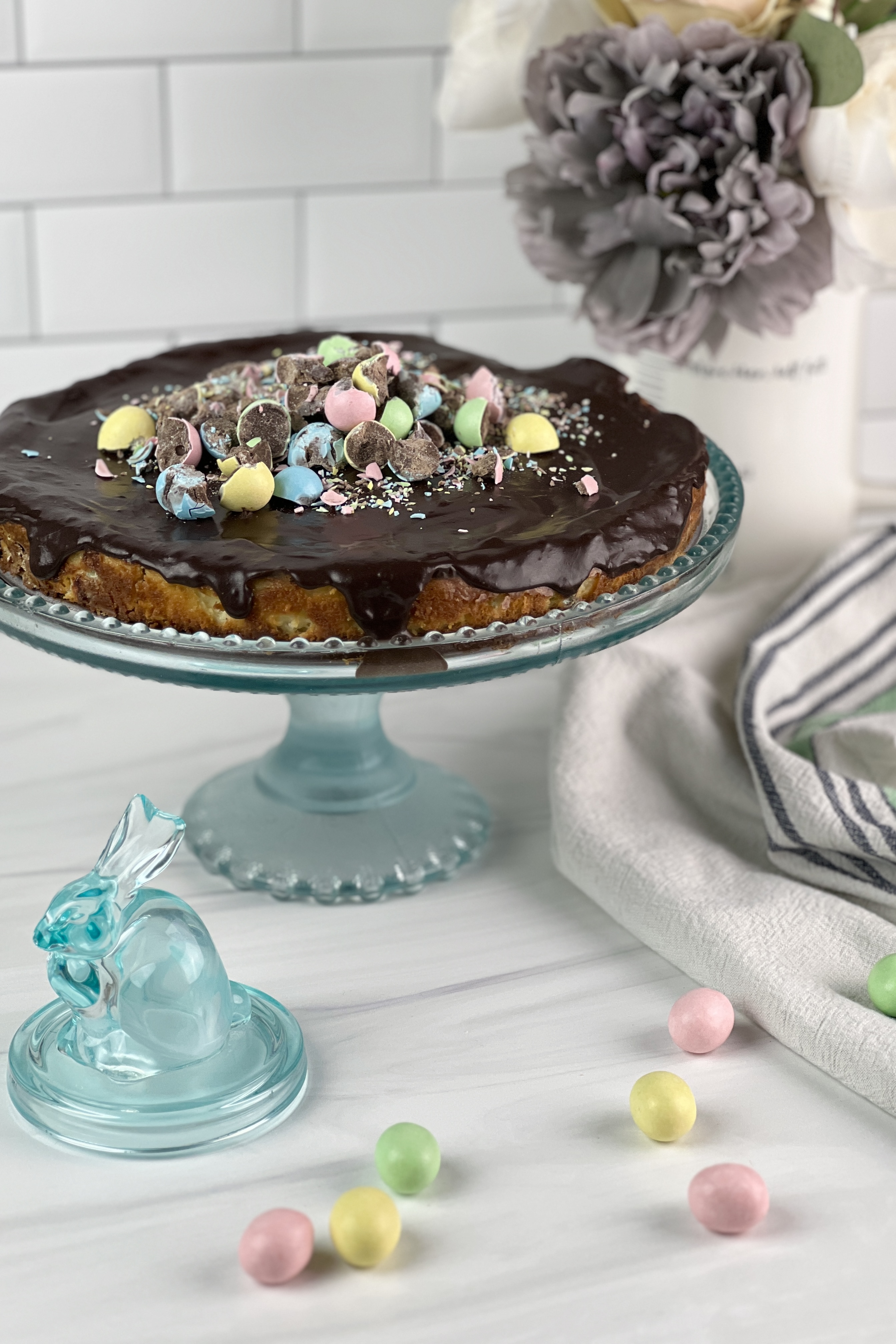 This creamy Easter egg cheesecake is packed with mini chocolate eggs, has a graham cracker crust, and is topped with chocolate ganache and mini chocolate eggs.