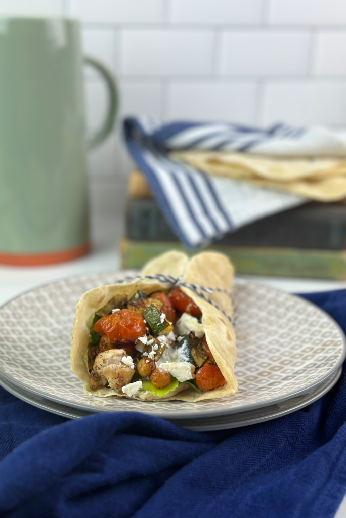 These Mediterranean Wraps feature a pita/tortilla stuffed with roasted vegetables, chickpeas, seasoned chicken, hummus, and a feta sauce.